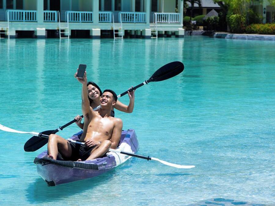Dos personas en un bote pequeño con remos, flotando en una piscina cristalina.