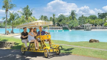 Un carruaje amarillo con toldo a rayas, cuatro pasajeros y vistas a una piscina y palmeras.
