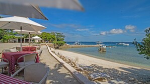 A beachside restaurant with outdoor seating, including tables and chairs, and a view of the sea.