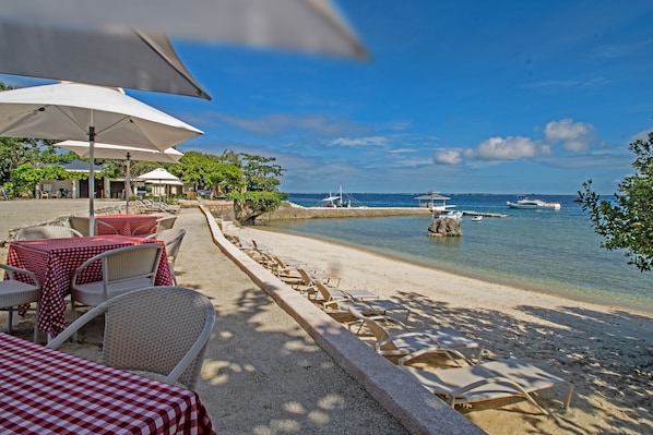 A beachside restaurant with outdoor seating, including tables and chairs, and a view of the sea. - Plantation Bay a Real Resort with a Real Spa (Lapu-Lapu)