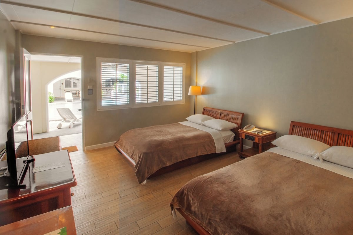 Ein Hotelzimmer mit zwei Betten, einem Schreibtisch, einer Lampe und einem Fenster mit Jalousien.