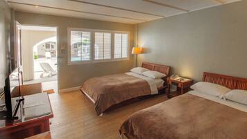 A hotel room with two beds, a desk, a lamp, and a window with blinds.