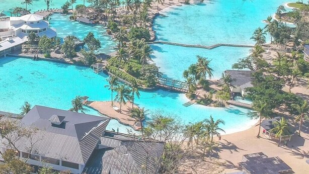 An aerial view of a resort with multiple swimming pools, beachfront villas, and a view of the ocean.