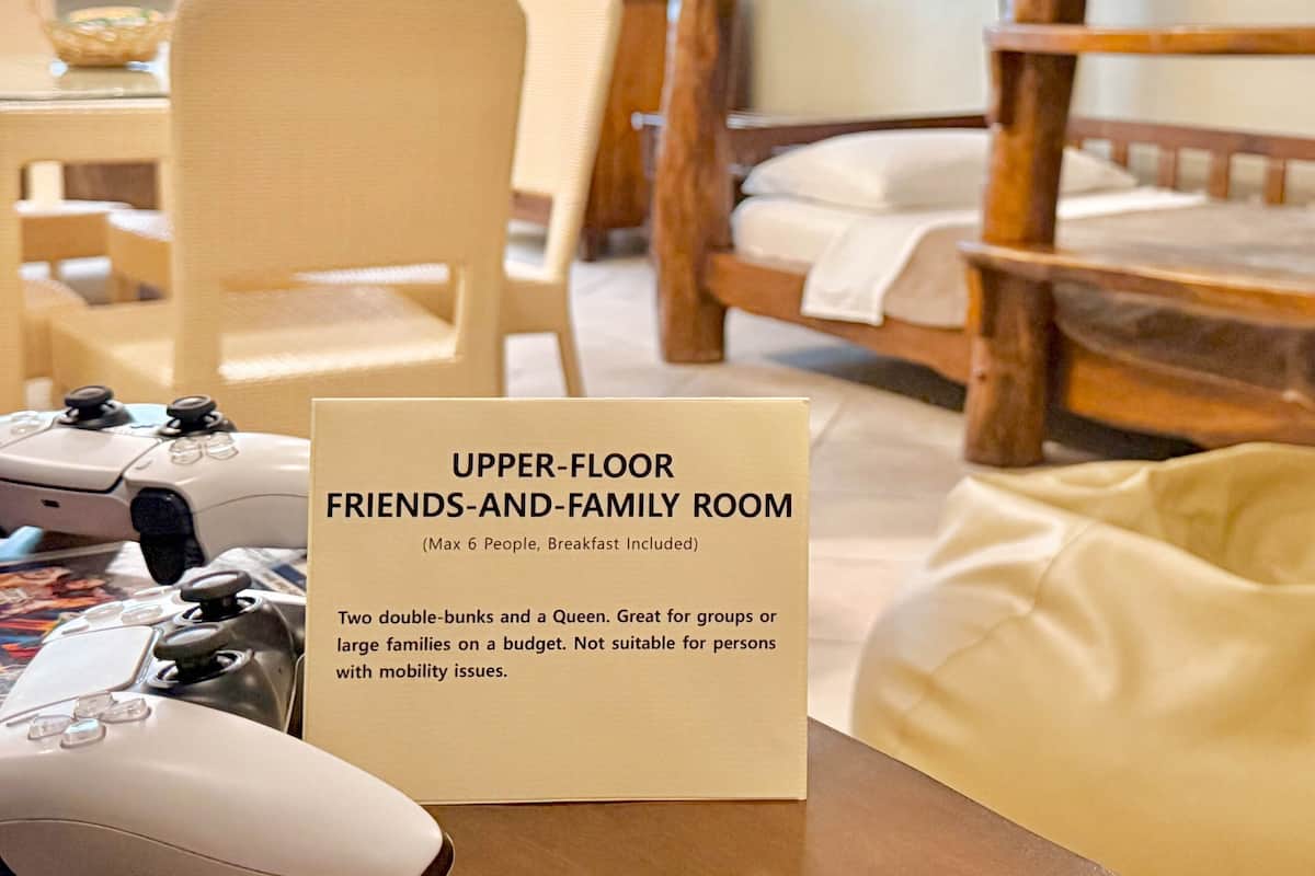 Ein Zimmer mit einem Bett, einem Sessel, einem Spielcontroller und einem Schild, das die Zimmerausstattung beschreibt.
