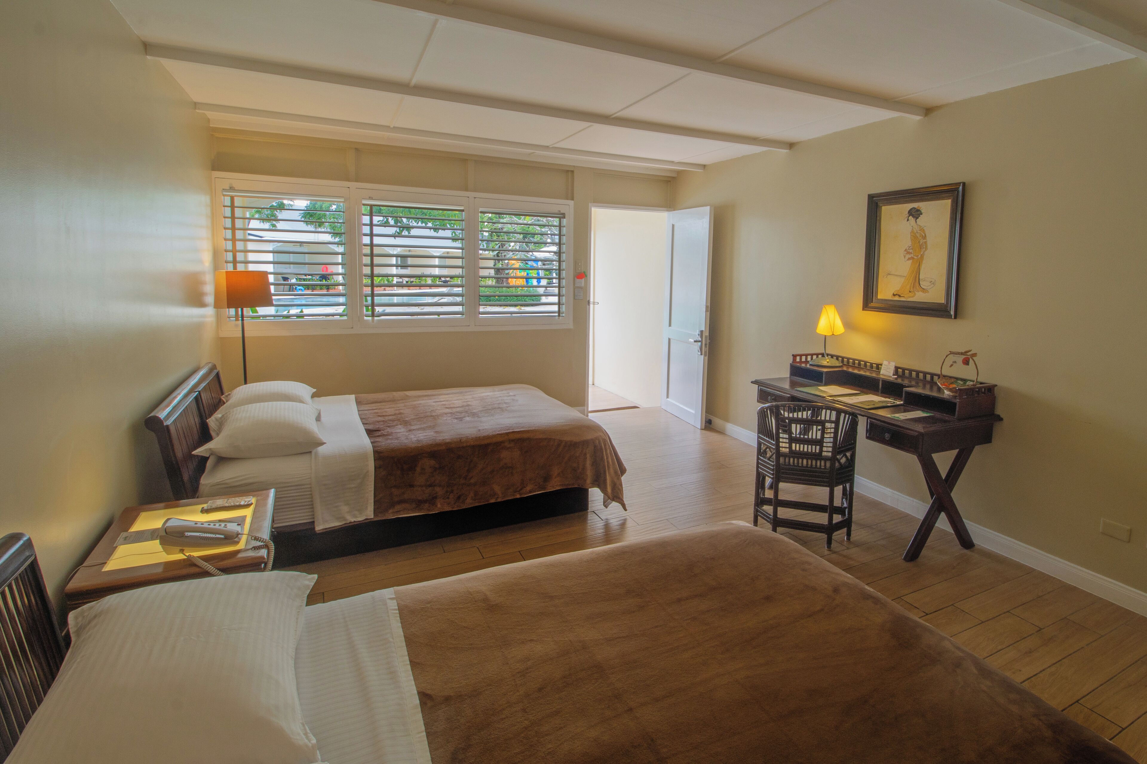 A hotel room with two beds, a desk with a chair, a lamp, and a framed picture on the wall.
