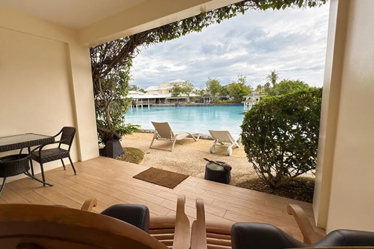 A patio with a table and chairs, a view of a pool, and lounge chairs.