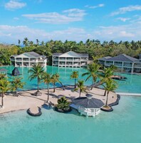 Um resort com vários edifícios, uma piscina grande e palmeiras.