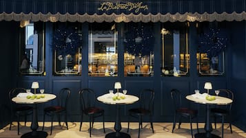 Un restaurante con fachada azul oscuro, cinco mesas con manteles blancos y sillas.