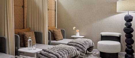 A modern hotel room with a sofa set, a small table with a vase, a lamp, and a textured rug.