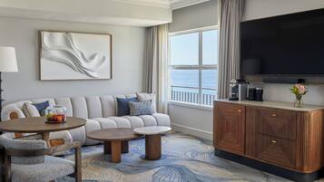 A modern living room with a sofa, two coffee tables, a TV, and a view of the sea.
