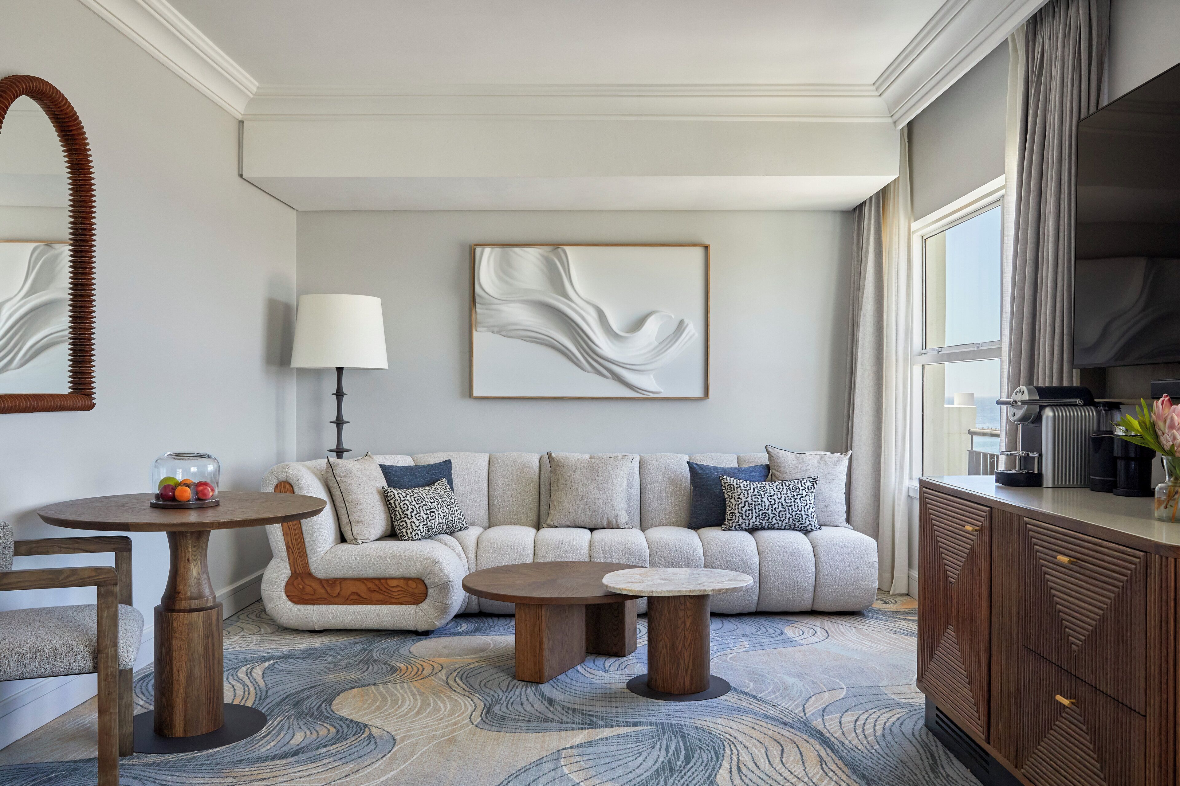 A modern living room with a sofa, two round tables, a coffee machine, and a large window.