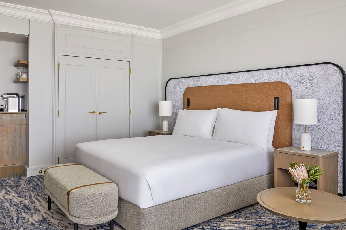 Une chambre d’hôtel bien aménagée, avec un grand lit, des tables de chevet, une petite table ronde et un banc.