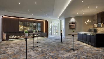 A modern hotel lobby with a reception desk, seating area, and a kitchen area.