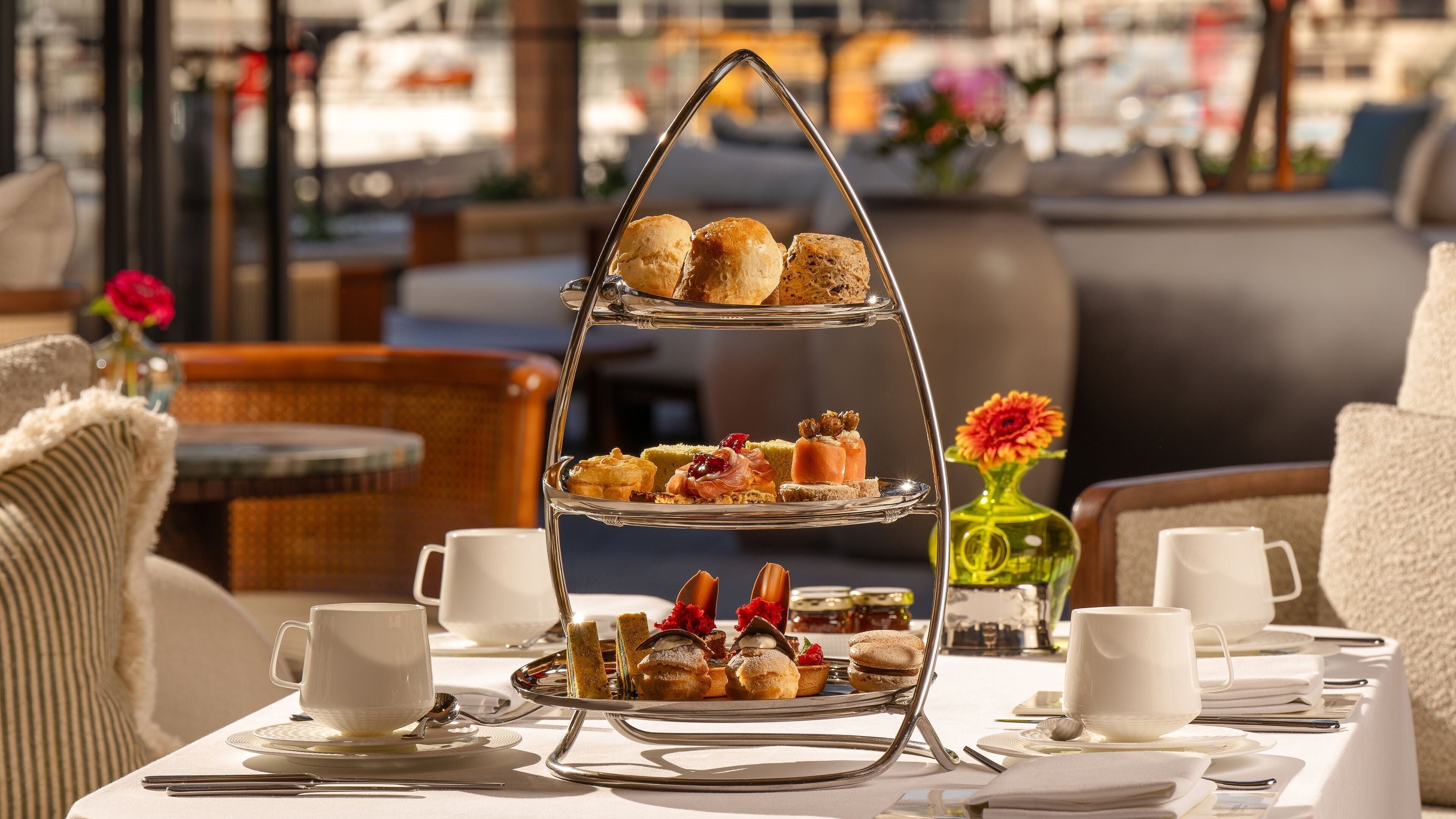 Un expositor escalonado para postres con pastelería y un jarrón de flores sobre una mesa.