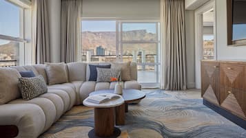 Une chambre d’hôtel moderne, dotée d’un grand canapé, de deux tables d’appoint et offrant une vue sur un paysage montagneux grâce à de grandes fenêtres.