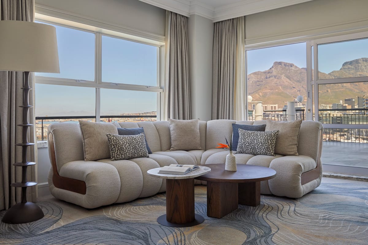 A modern living room with a sectional sofa, a round coffee table, and a view of a mountainous landscape through large windows.
