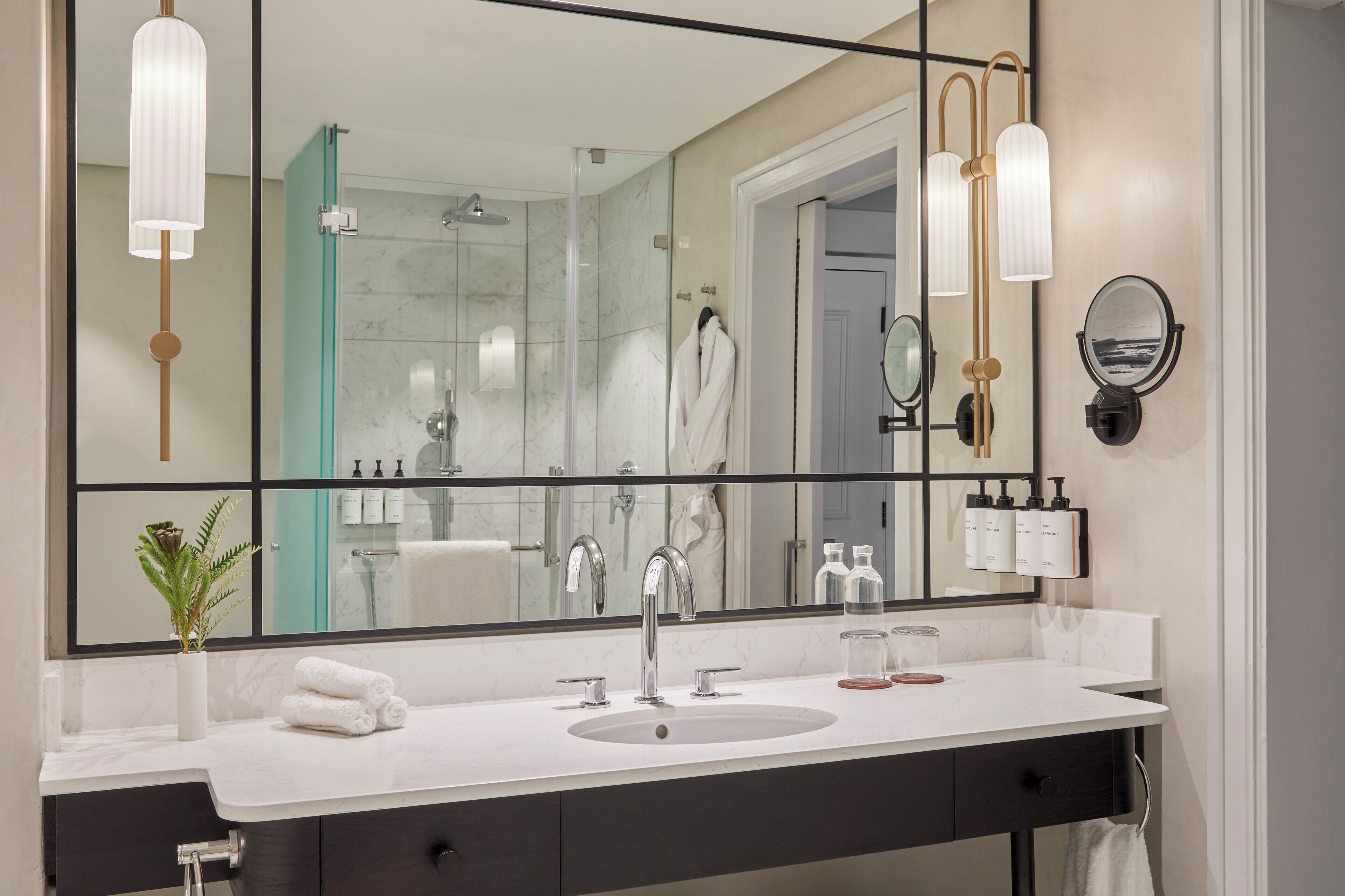 A modern bathroom with a large mirror, a sink, and a glass-enclosed shower.