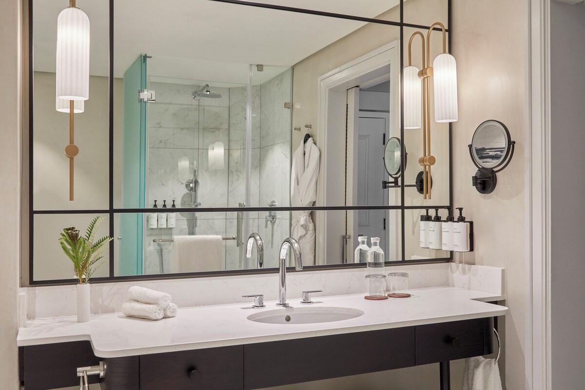 A modern bathroom with a large mirror, a sink, and a glass-enclosed shower.