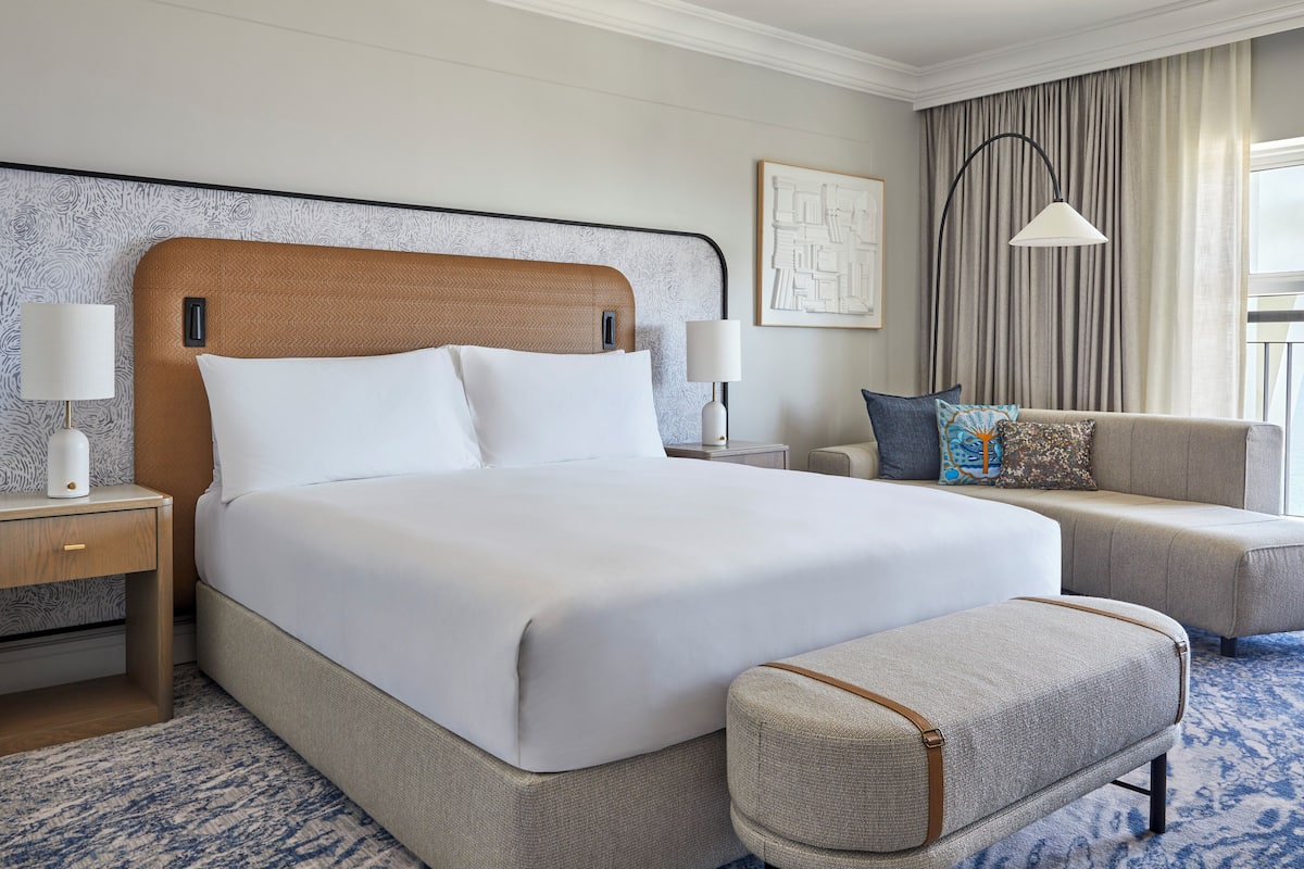 A hotel room with a large bed, a sofa, a side table, and a lamp.