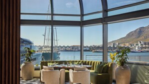 A restaurant with a checkered floor, green sofa, and chairs, overlooking a harbor with boats and buildings. - InterContinental Table Bay Cape Town by IHG (Cape Town)