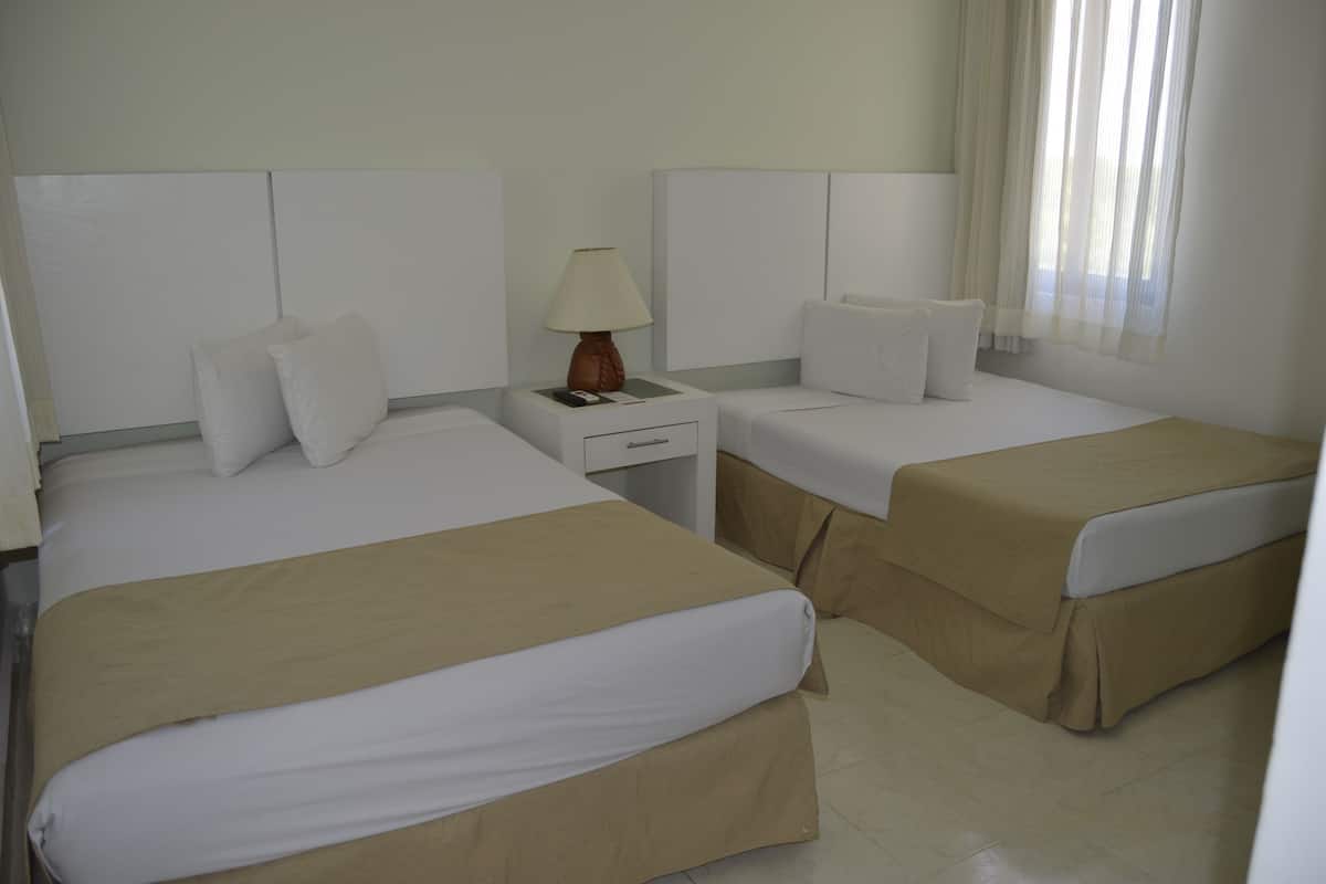 Een hotelkamer met twee bedden, een nachtkastje met een lamp en een raam met dunne gordijnen.