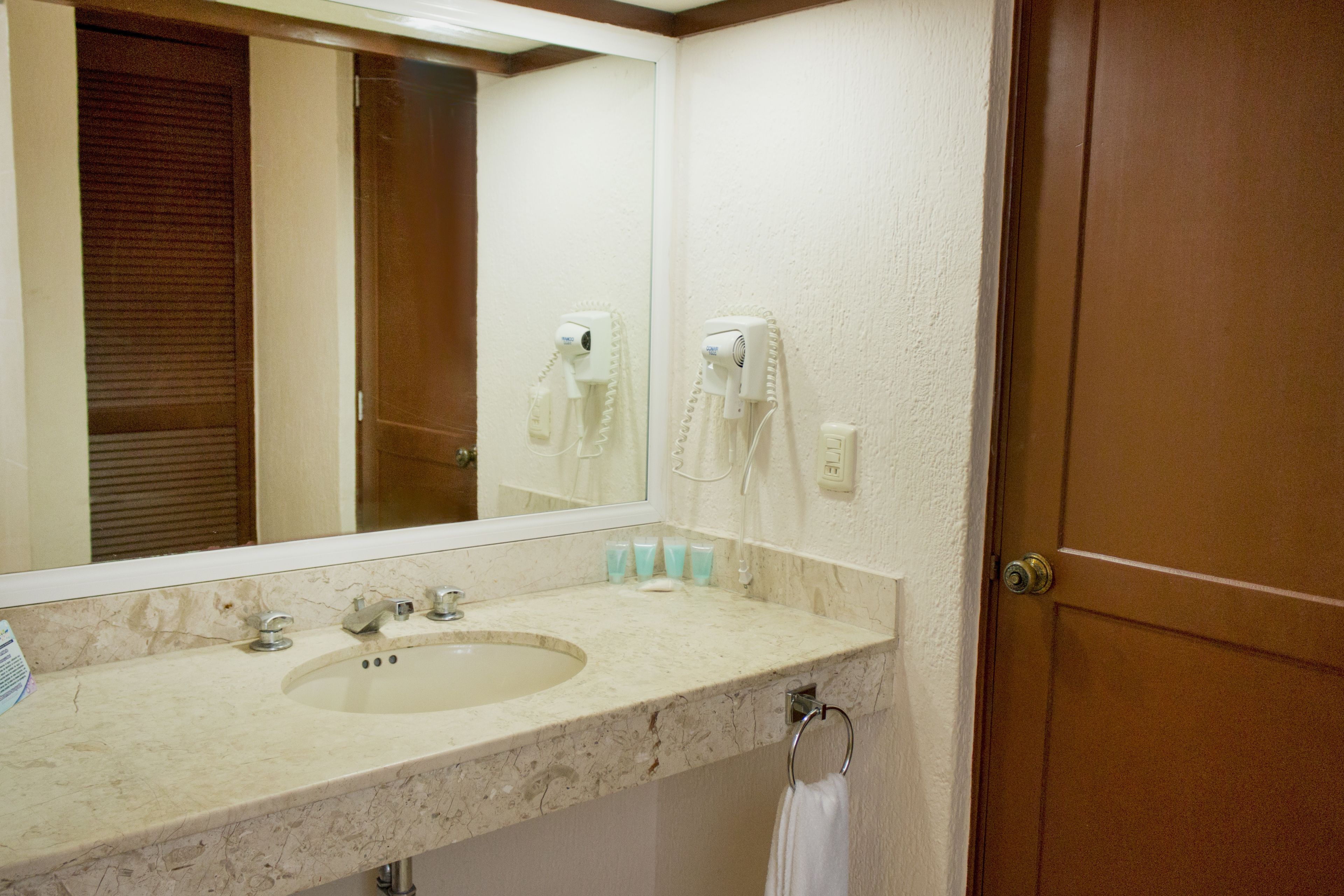 A bathroom with a marble sink, a mirror, a hairdryer, and a towel ring.