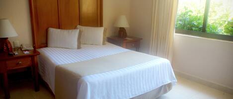 Ein Hotelzimmer mit einem großen Bett, zwei Nachttischen, einer Lampe und einem Fenster mit Vorhängen.