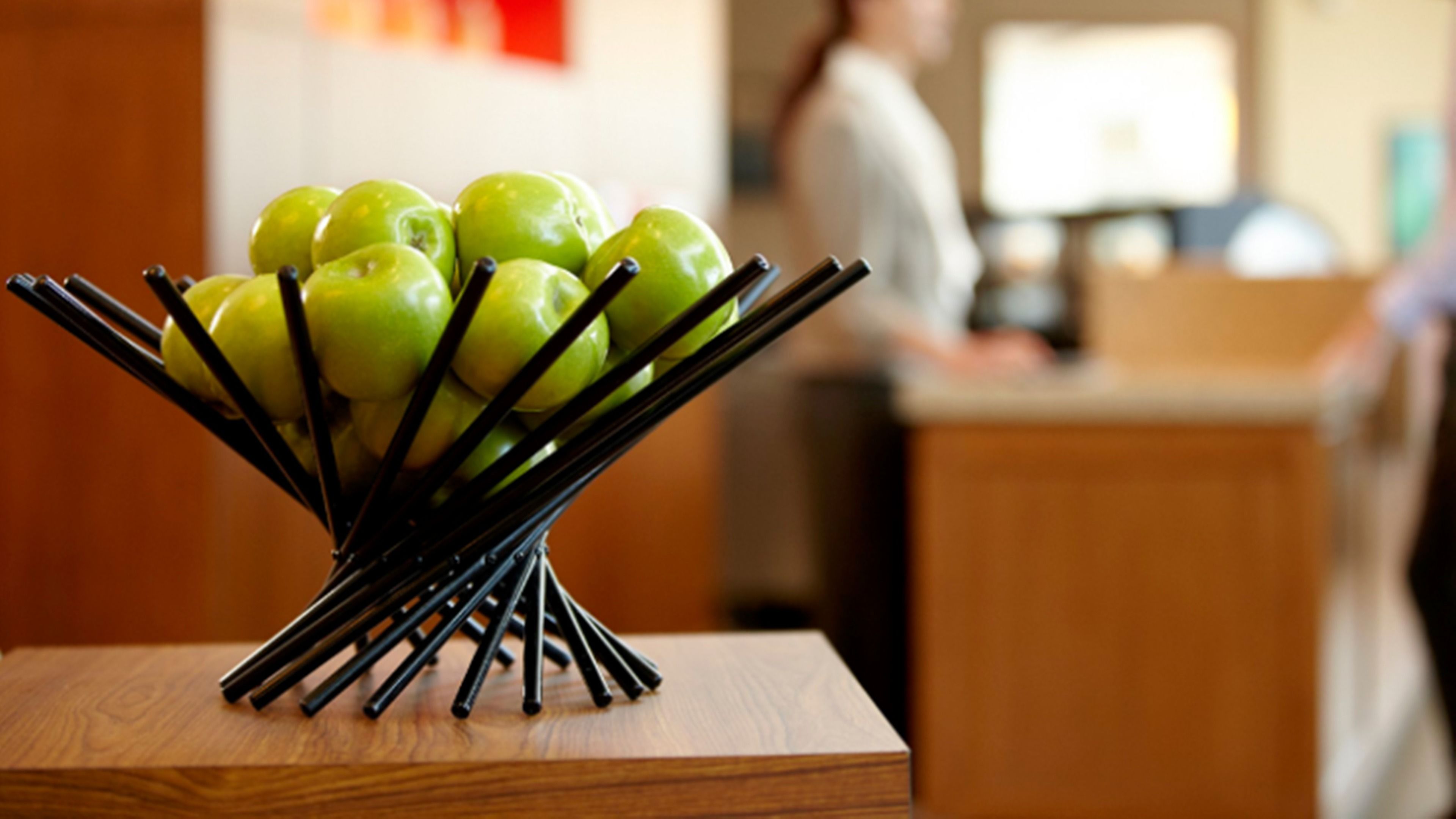 Una mesa de madera con un soporte metálico negro que sostiene varias manzanas verdes.