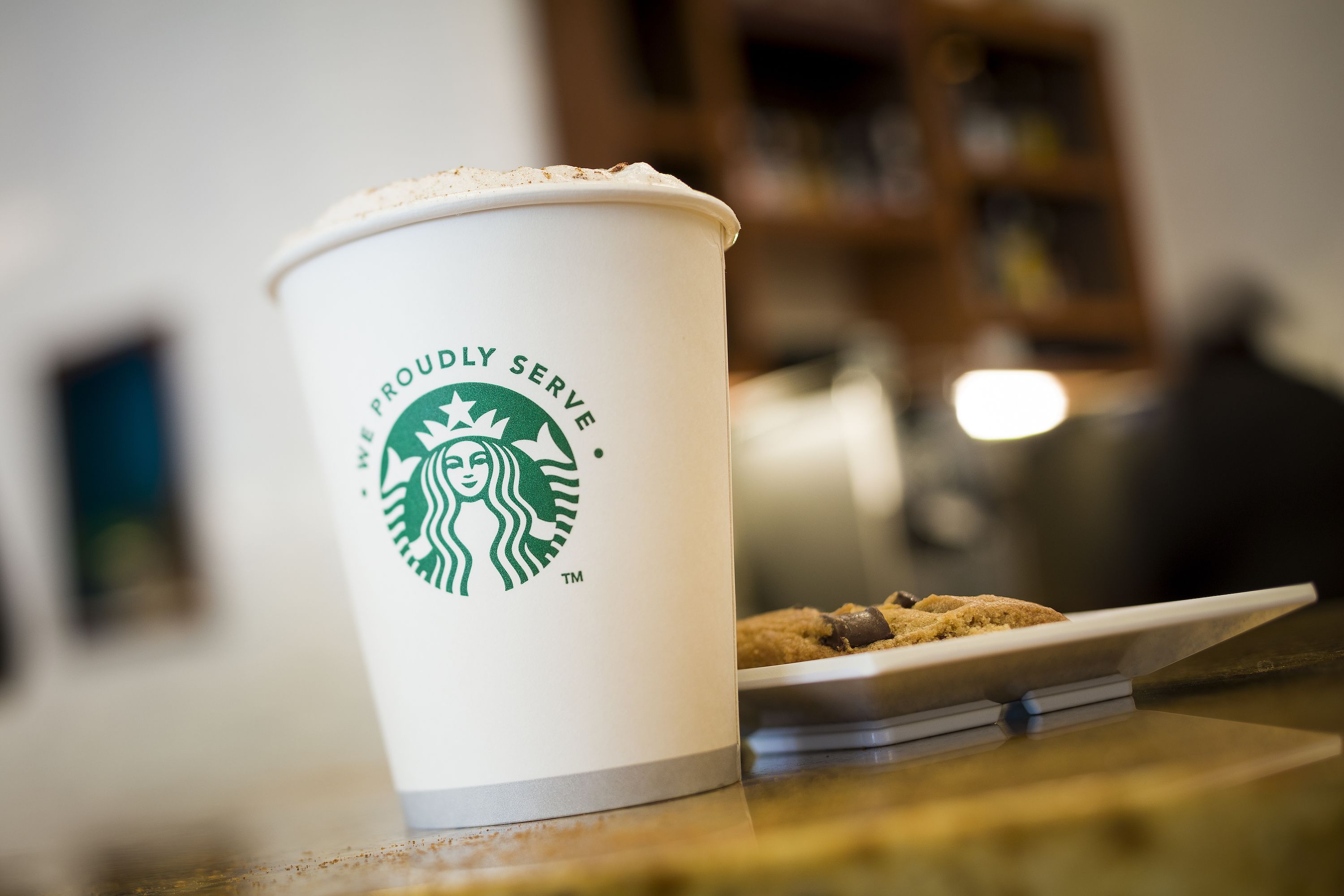Une tasse de Starbucks avec un biscuit posé sur une table.