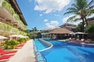 Área de piscina em resort com espreguiçadeiras e guarda-sóis, cercada por palmeiras e um céu claro.