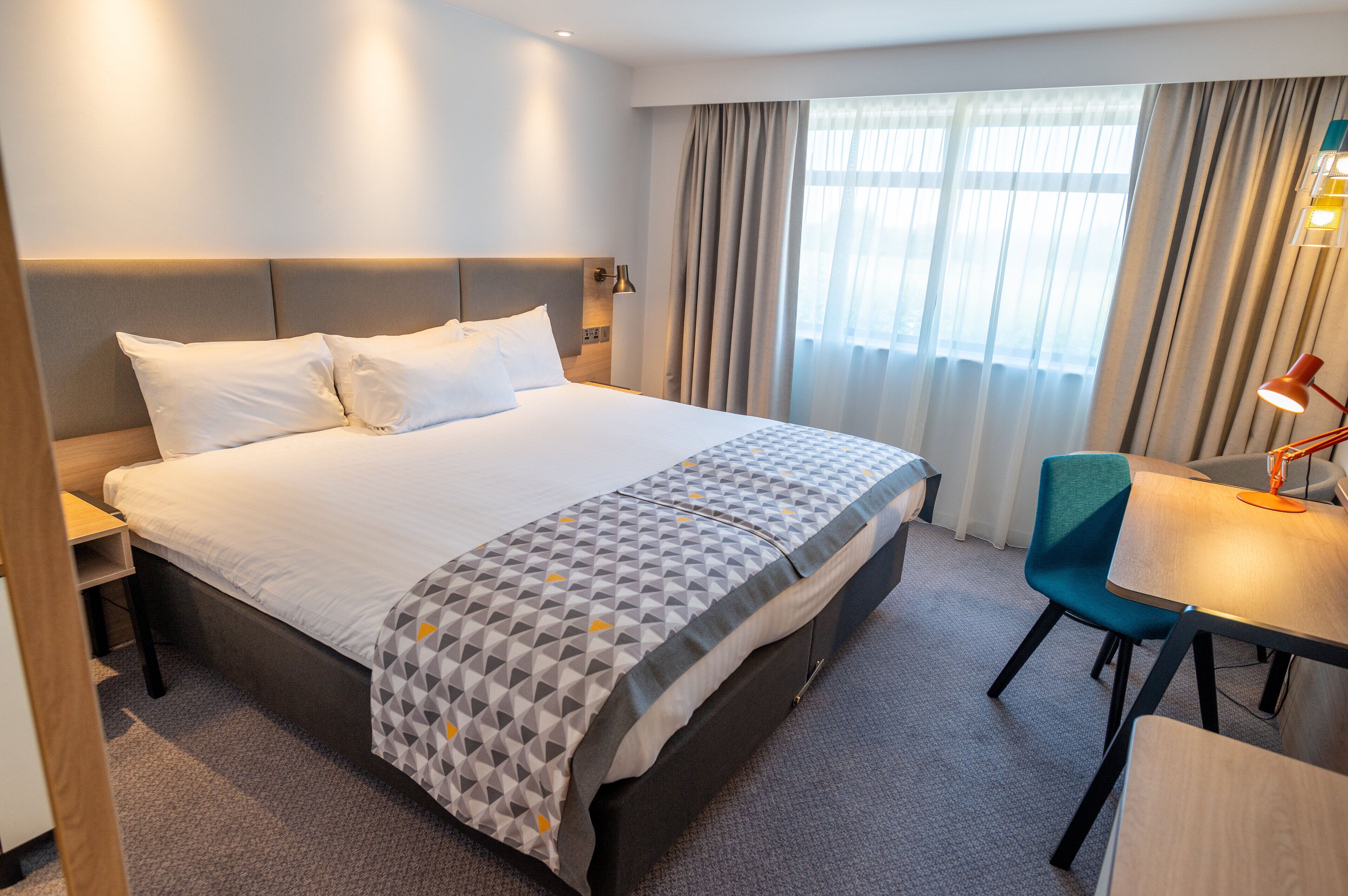 Een hotelkamer met een groot bed, een bureau met een stoel, en een raam met gordijnen.