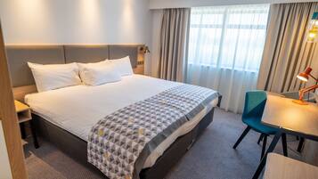 Een hotelkamer met een groot bed, een bureau met een stoel, en een raam met gordijnen.