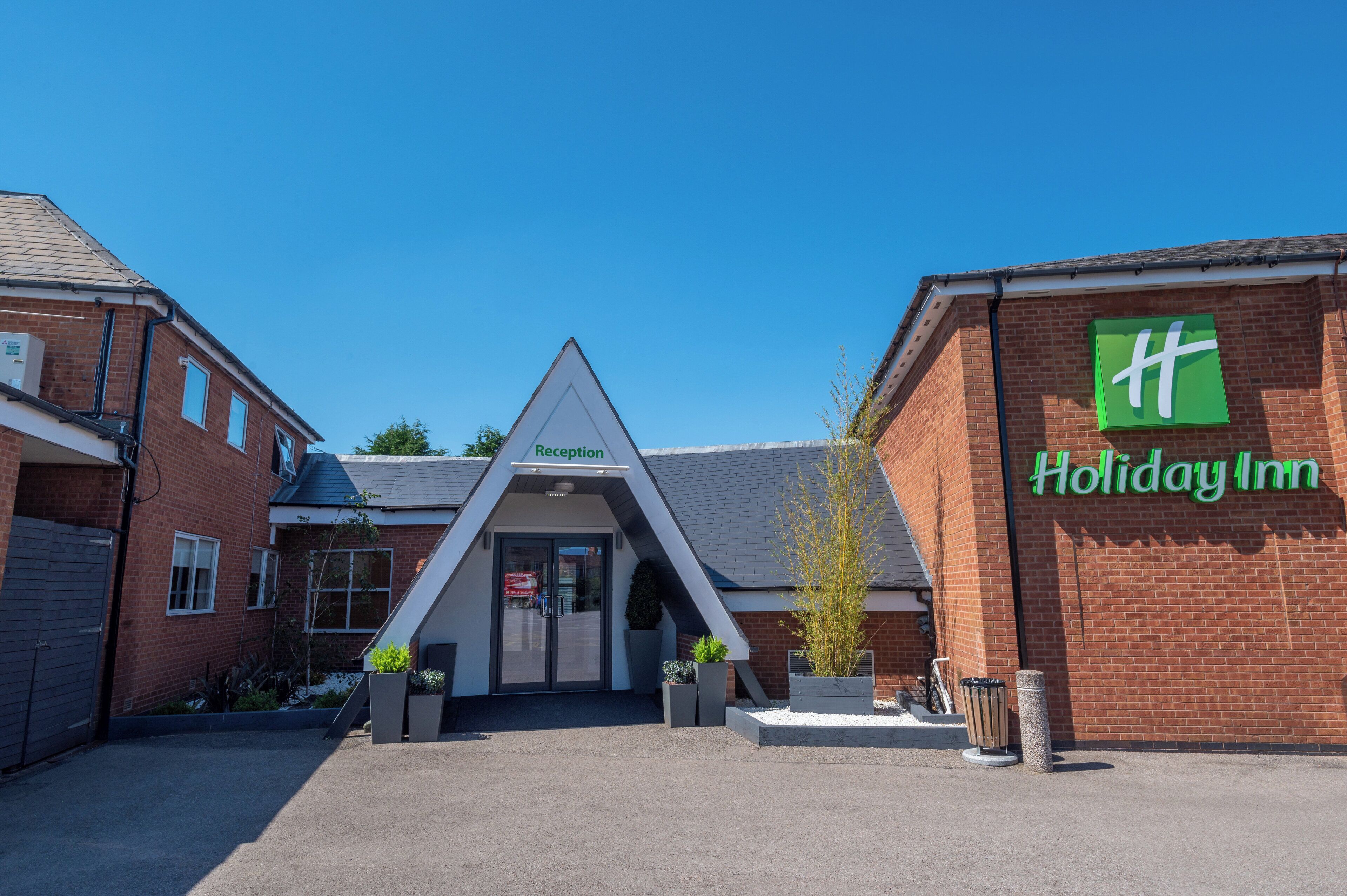 Zona de recepción de Holiday Inn, con cielo despejado, un mostrador de recepción y fachada de edificio de ladrillo.