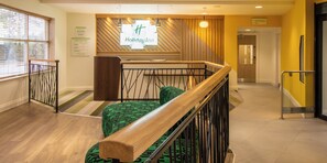 A hotel lobby with a reception desk, a staircase with a wooden handrail, and a green patterned sofa. - Holiday Inn Leicester - Wigston by IHG (Wigston)