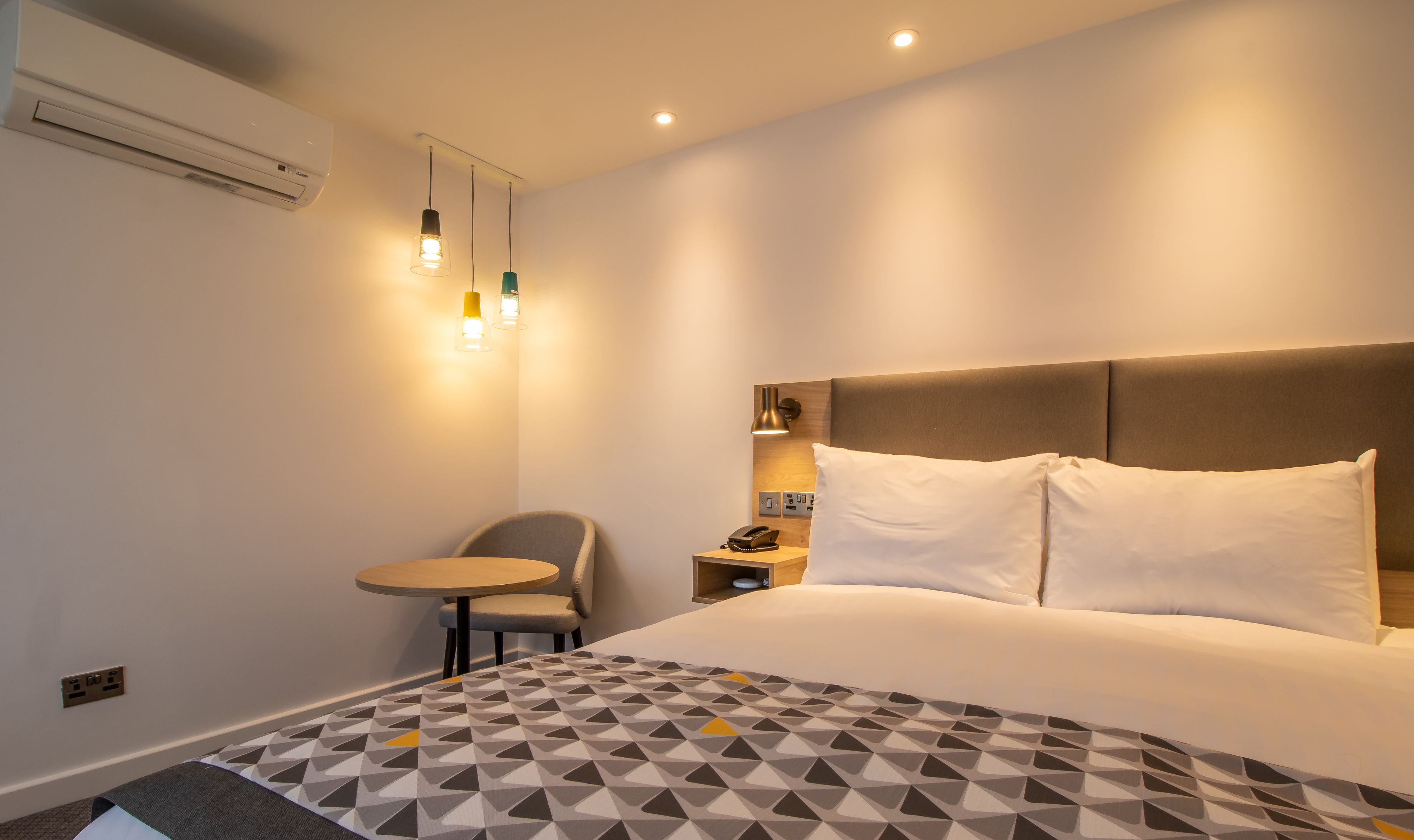 Ein Hotelzimmer mit Bett, Nachttisch, Sessel und einem kleinen Tisch mit Lampe.