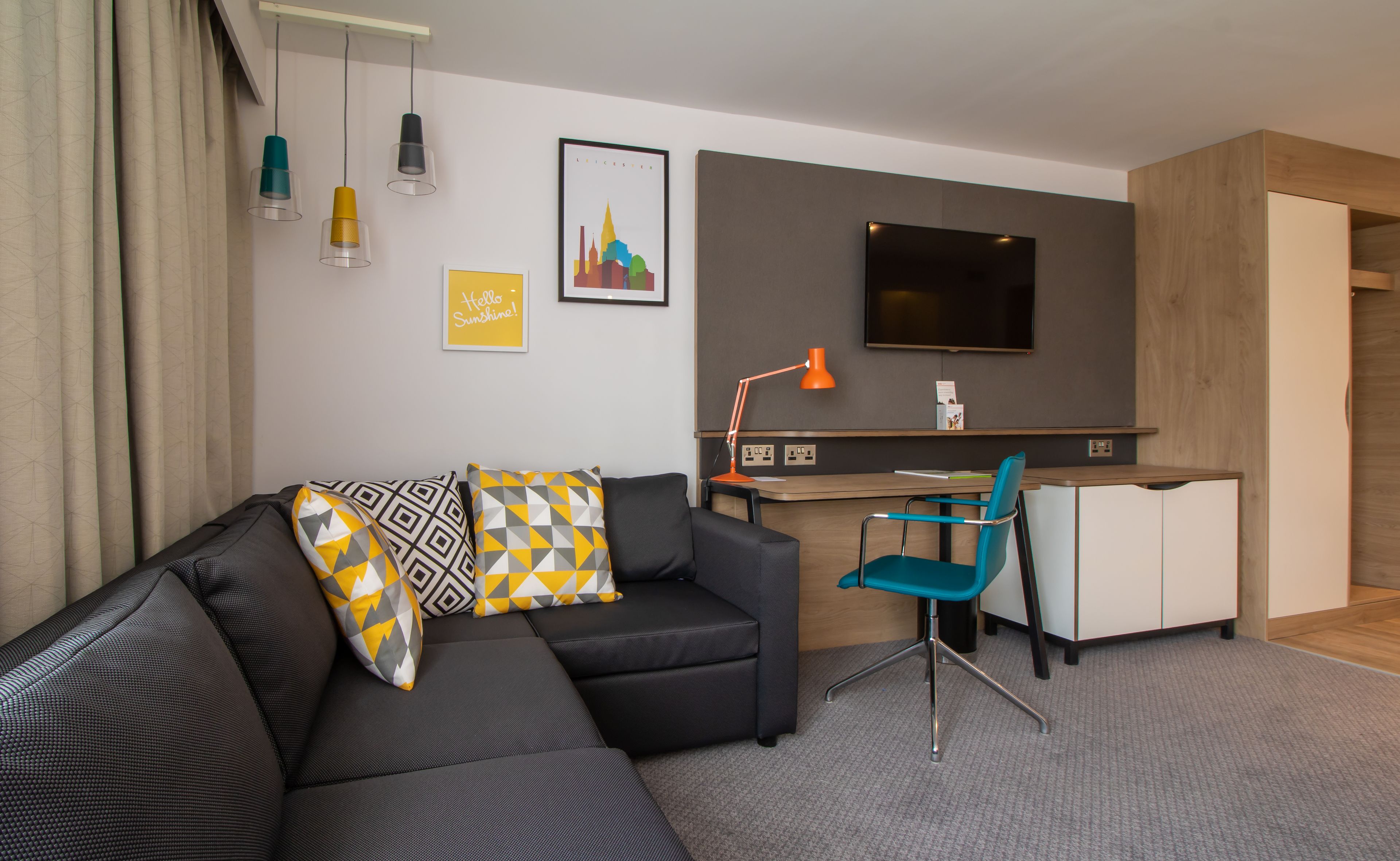 Un salon moderne avec un canapé d’angle, un bureau avec un ordinateur, un téléviseur et un fauteuil.