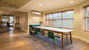 A conference room with a long table, green chairs, and large windows with blinds. - Holiday Inn Leicester - Wigston by IHG (Wigston)