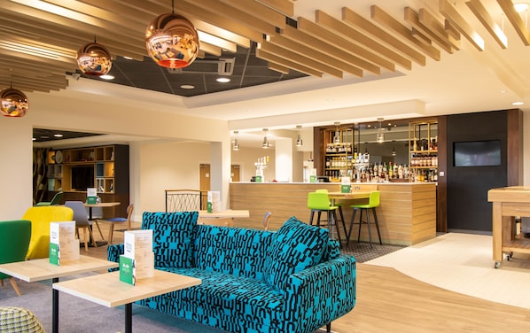 A modern lounge area with a bar, seating, and a patterned sofa.