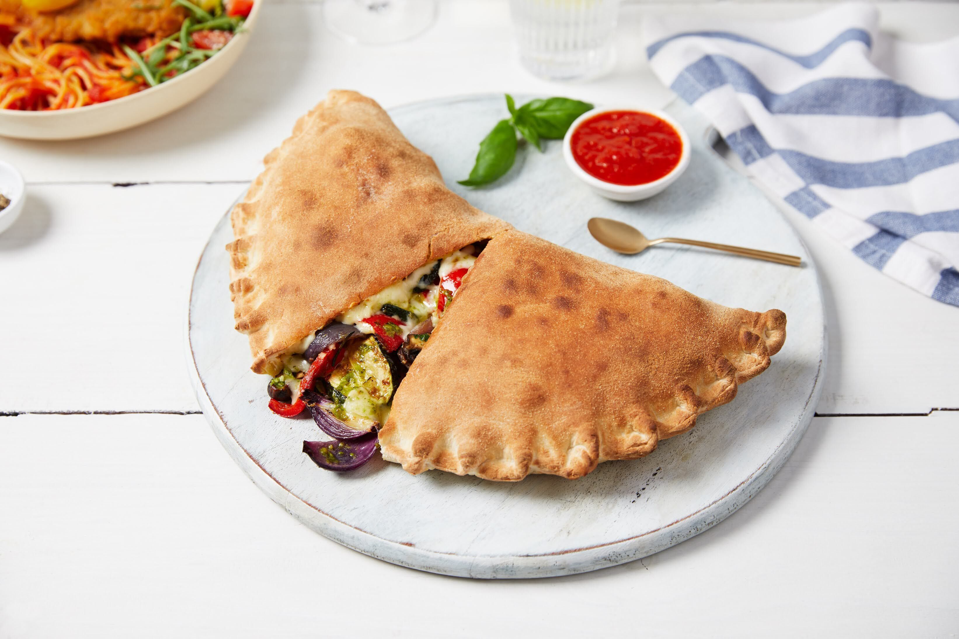Eine angebrochene Empanada auf einem Teller, zusammen mit einer Saucenschale und einem Löffel in der Nähe.