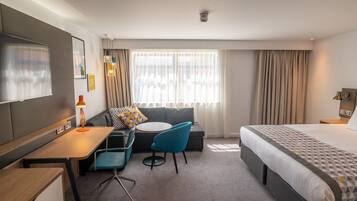 A hotel room with a bed, a desk, a chair, a sofa, and a window with curtains.
