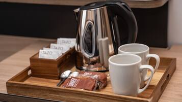 A tray with a coffee maker, two white mugs, and a wooden box containing coffee pods and a packet of biscuits.