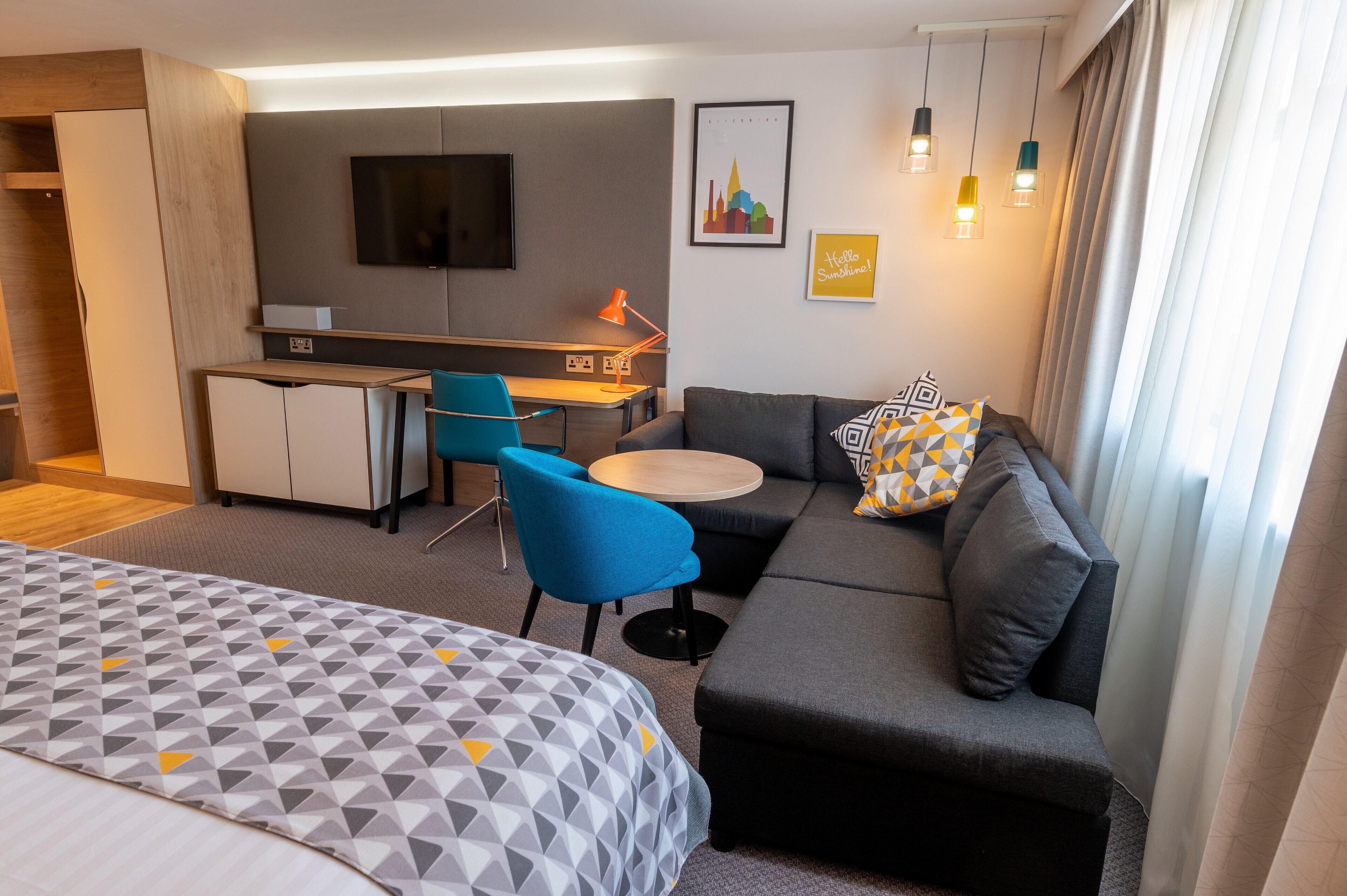 A modern hotel room with a sofa, a bed, a desk, and a chair.