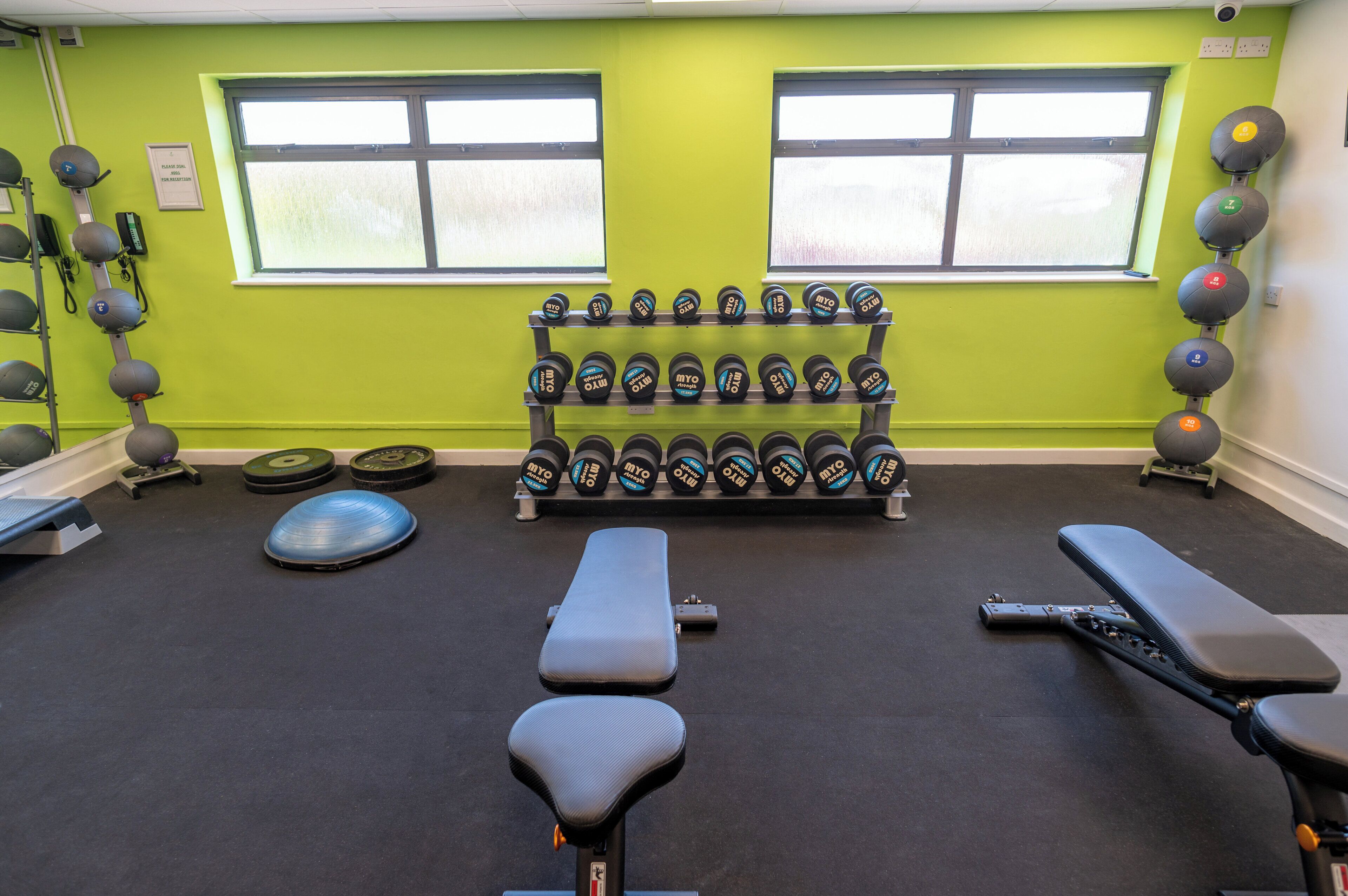 Un gimnasio con equipo de ejercicio, bancos y mancuernas.