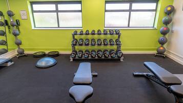 Un gimnasio con equipo de ejercicio, bancos y mancuernas.