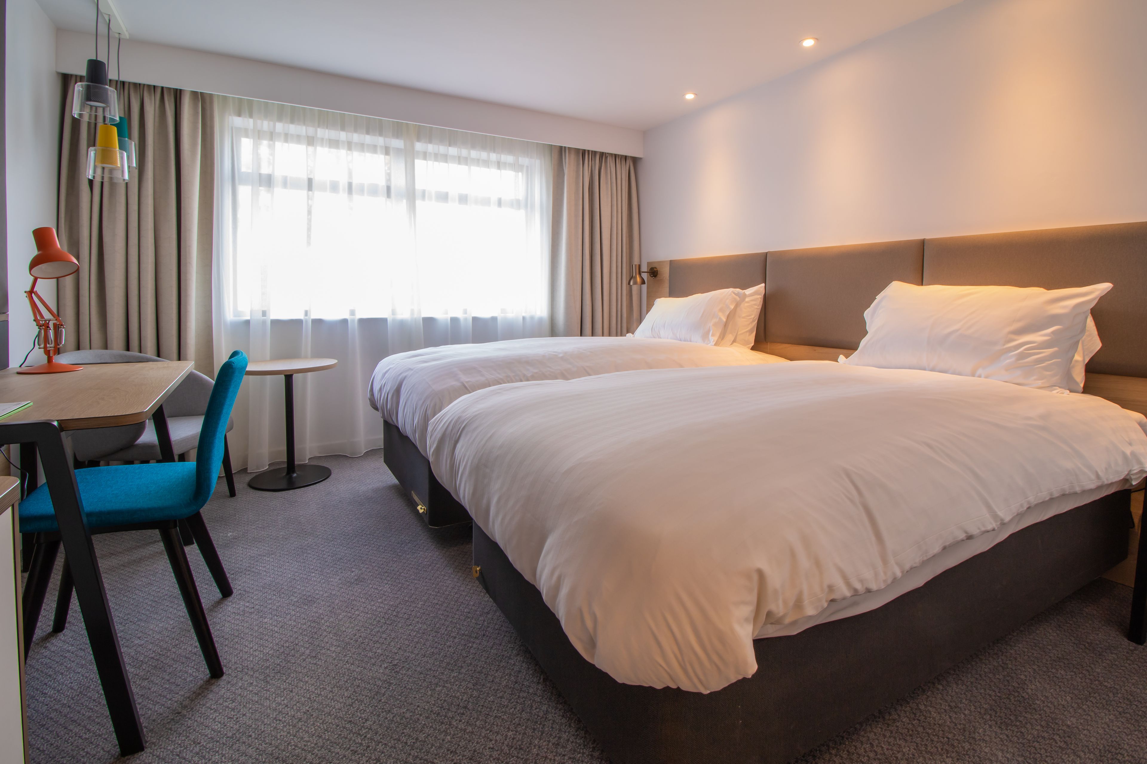 Een hotelkamer met een groot bed, een bureau met stoel en een raam met gordijnen.