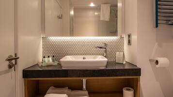 Une salle de bain avec un lavabo blanc, un miroir, un porte-serviettes et une étagère contenant des serviettes et des articles de toilette.