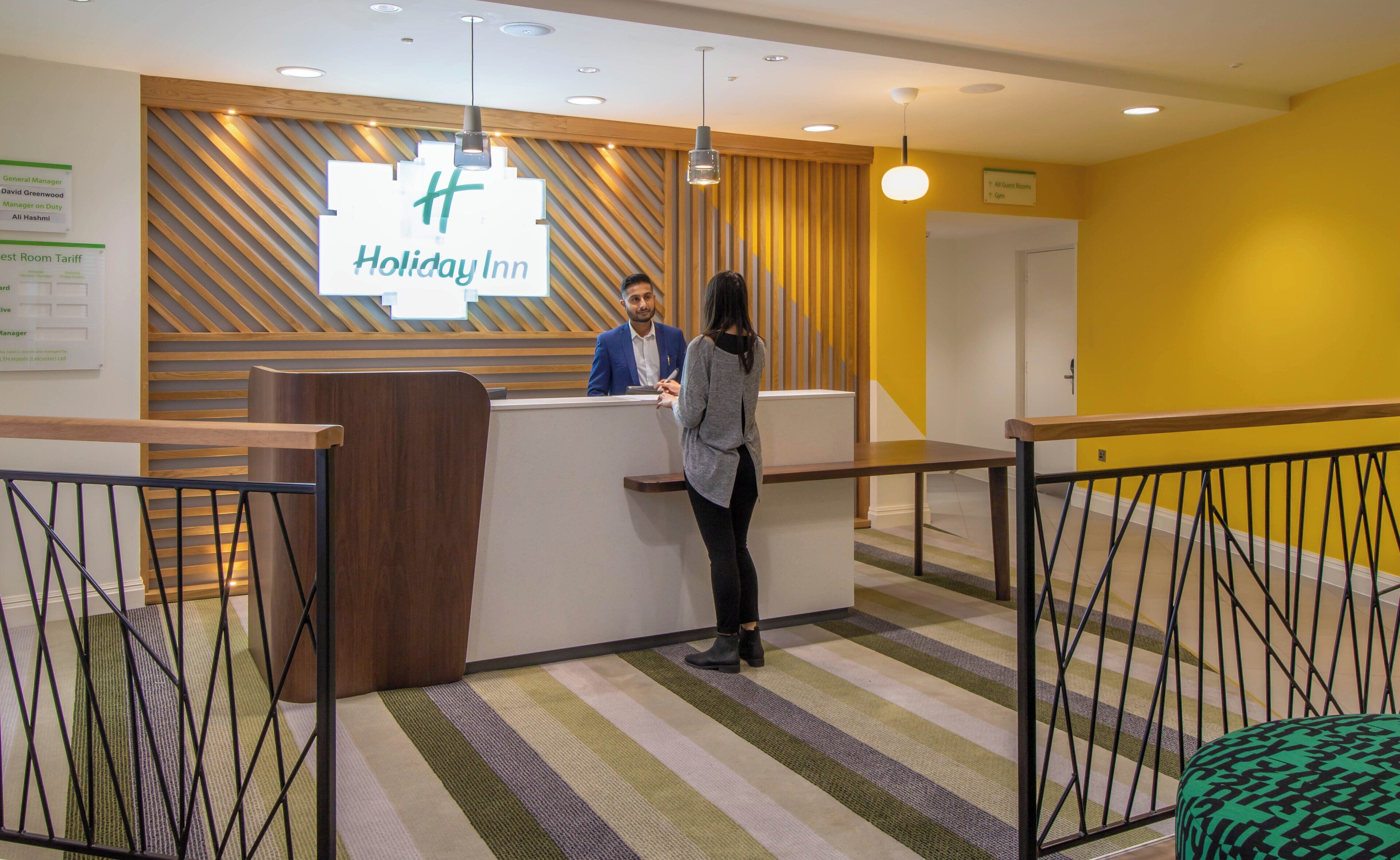 Un comptoir d’accueil avec une enseigne indiquant « Holiday Inn », et un homme et une femme debout derrière le comptoir.