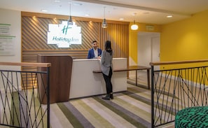 A reception desk with a sign reading 'Holiday Inn' and a man and woman standing at the counter. - Holiday Inn Leicester - Wigston by IHG (Wigston)