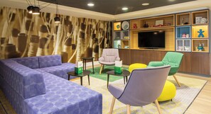 A modern living room with a sectional sofa, a flat-screen TV, and a variety of decorative items on shelves. - Holiday Inn Leicester - Wigston by IHG (Wigston)