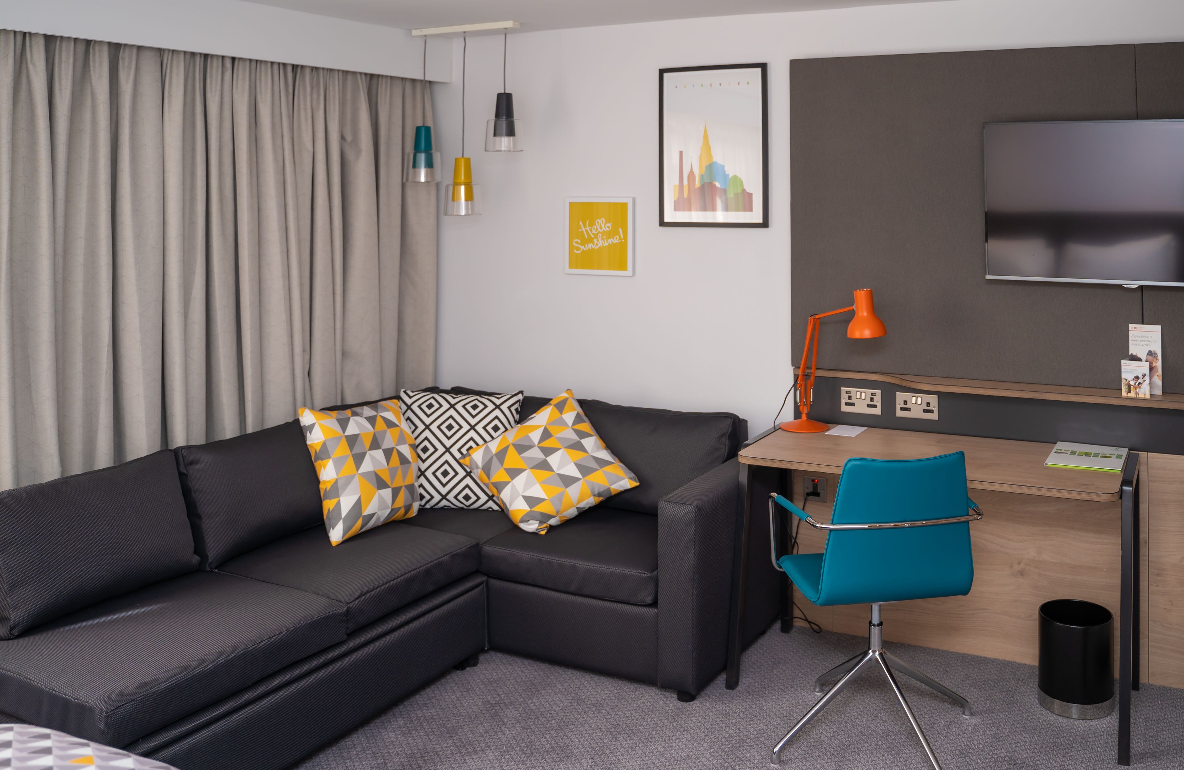 A modern hotel room with a sofa, a desk, a chair, a TV, and a curtain.